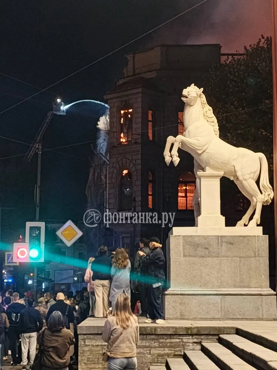 Пожарные применяют высотное оборудование и проливают воду на горящее здание; огонь на нижних этажах ослабел, особенно на первом и втором.